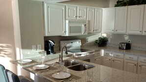 A modern kitchen with white cabinets, a granite countertop, and a central island with bar stools. - Oceanfront Gem Clean 1080sf New Furniture, Beds, Carpet Free WiFi Cable Gym Park (Myrtle Beach)