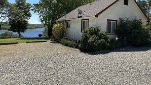 A single-story house with a sloped roof, surrounded by gravel driveway, trees, and a lake view. - Clean, Family/Pet Friendly Lake View, 2-Bdrm Cabin Near Several Marinas/launches (Gamaliel)