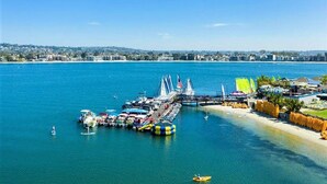 Een jachthaven met aangemeerde boten, een steiger die in het water reikt, en een strand met parasols en ligbedden.