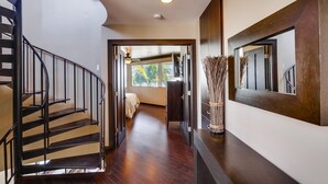 Een modern interieur met een gebogen trap, een grote spiegel en uitzicht op een kamer met een bed en raam.