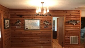 L’intérieur d’un chalet en rondins, avec des murs en bois, une carte, des panneaux indiquant la présence de poissons et un poisson empaillé accroché au mur.
