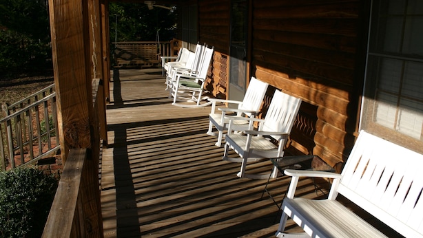 Une véranda en bois avec des fauteuils Adirondack blancs et une terrasse en bois.