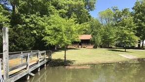 Un pont en bois enjambe un étang, avec un bâtiment visible au loin.