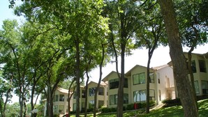 A row of modern multi-story buildings with large windows, surrounded by well-maintained lawns and trees.