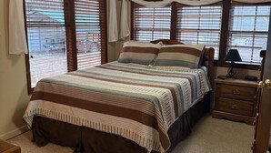 A bedroom with a large bed, a nightstand, a dresser, and a window with blinds.