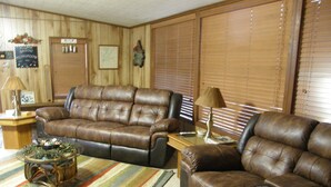 A living room with a brown leather sectional sofa, a coffee table with a striped rug, and a wooden wall with a welcome sign.