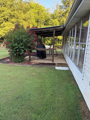 A covered patio with a grill, a small table, and a bench. - Lodging on Reelfoot Lake Upper Blue Basin at The Bayou Bungalow (Union City)
