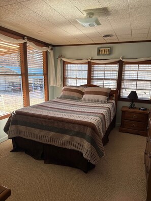 A bedroom with a large bed, wooden headboard, a nightstand, and a window with blinds. - Lodging on Reelfoot Lake Upper Blue Basin at The Bayou Bungalow (Union City)