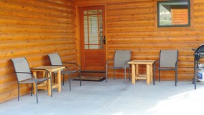 A log cabin with a wooden exterior, a glass door, and a small patio area with two tables and four chairs. - THE EAGLES NEST with SPECTACULAR MOUNTAIN & YELLOWSTONE RIVER VIEWS  (Gardiner)