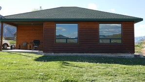 A wooden cabin with a large window, a covered patio, and a car parked outside. - THE EAGLES NEST with SPECTACULAR MOUNTAIN & YELLOWSTONE RIVER VIEWS  (Gardiner)