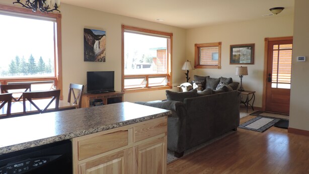 A spacious living area with a kitchen island, a dining table, and a sofa. There are large windows providing natural light and a view of the outdoors. - THE EAGLES NEST with SPECTACULAR MOUNTAIN & YELLOWSTONE RIVER VIEWS  (Gardiner)