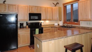 A kitchen with wooden cabinets, a black refrigerator, a microwave, a stove, and a granite countertop. - THE EAGLES NEST with SPECTACULAR MOUNTAIN & YELLOWSTONE RIVER VIEWS  (Gardiner)