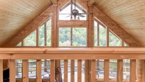 Ein Dachzimmer aus Holz mit geneigter Decke, großen Fenstern und einem Deckenventilator.