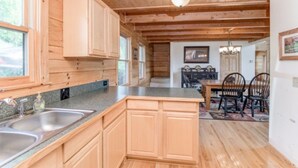 Ein Holzblockhaus-Interieur mit Küchenbereich, der zwei Spülen, Holzschränke und einen Esstisch mit Stühlen umfasst.