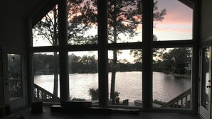 Ein geräumiges Zimmer mit großen Fenstern und Blick auf einen See, eine Holzterrasse und eine Treppe zu einem Außenbereich.