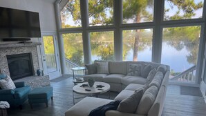 Ein geräumiges Wohnzimmer mit einer großen Eckcouch, einem Kamin, einem Flachbildfernseher und Seeblick durch große Fenster.