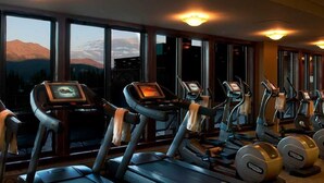 Ein Fitnessraum mit Laufbändern und Crosstrainern, großen Fenstern mit Bergblick und Deckenleuchten.