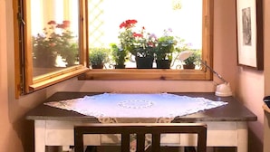 A small dining area with a table, chairs, a window with a view of flowers and a building, and a mirror on the wall.