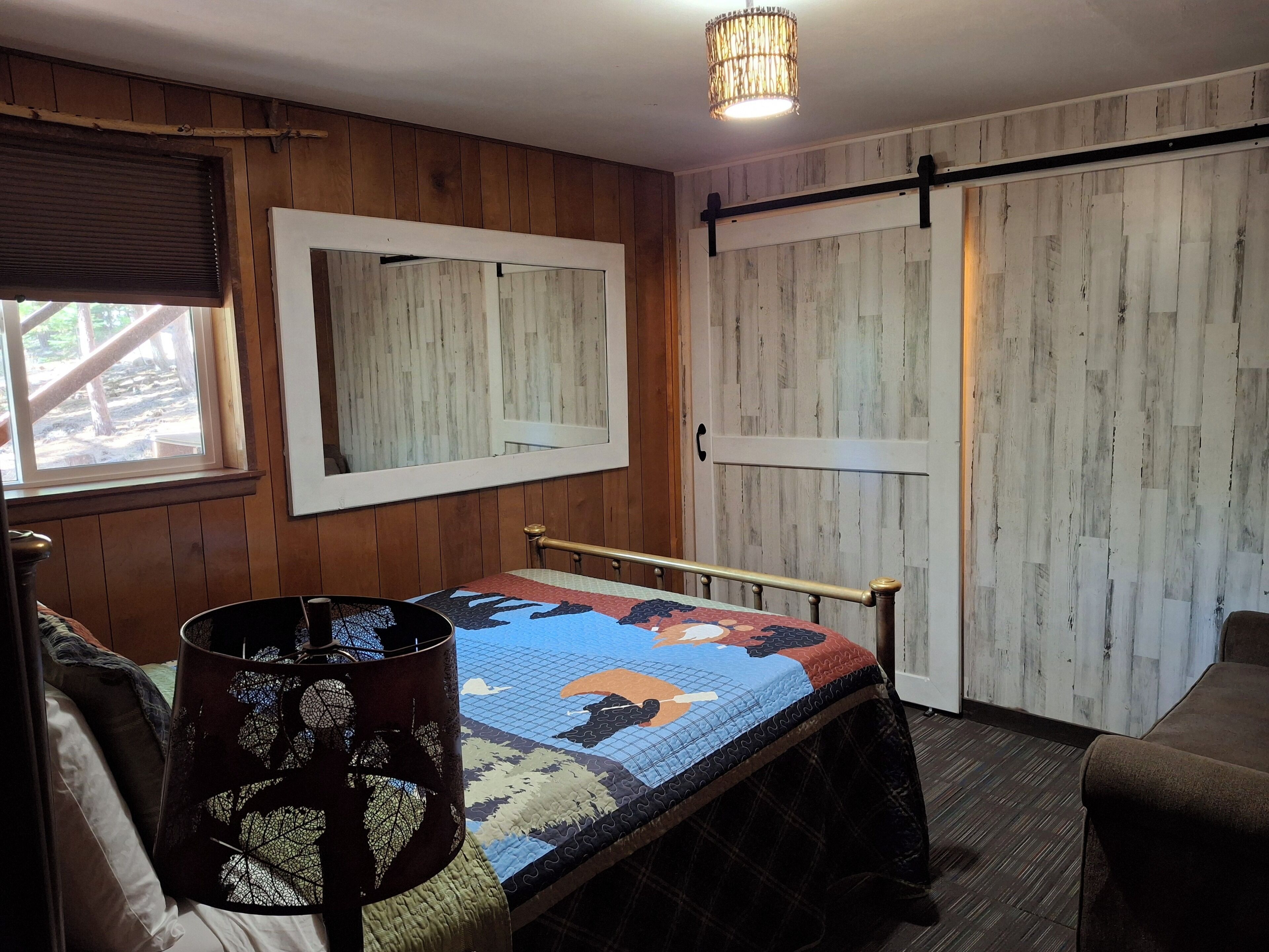 A cozy room with a bed, a window, a mirror, and a door.