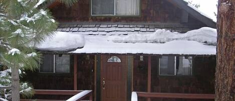 Una cabaña rústica con fachada de madera, un porche cubierto y techo nevado.