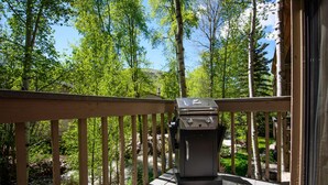 Eine Holzterrasse mit Grill, mit Blick auf eine bewaldete Landschaft und einen Fluss.
