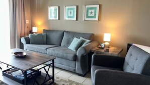 A living room with a grey sofa, a coffee table, and two lamps. There are three framed pictures on the wall. - GULF FRONT - GREAT VIEWS - Direct Walk Out - Only Steps to Private Beach (Inlet Beach)