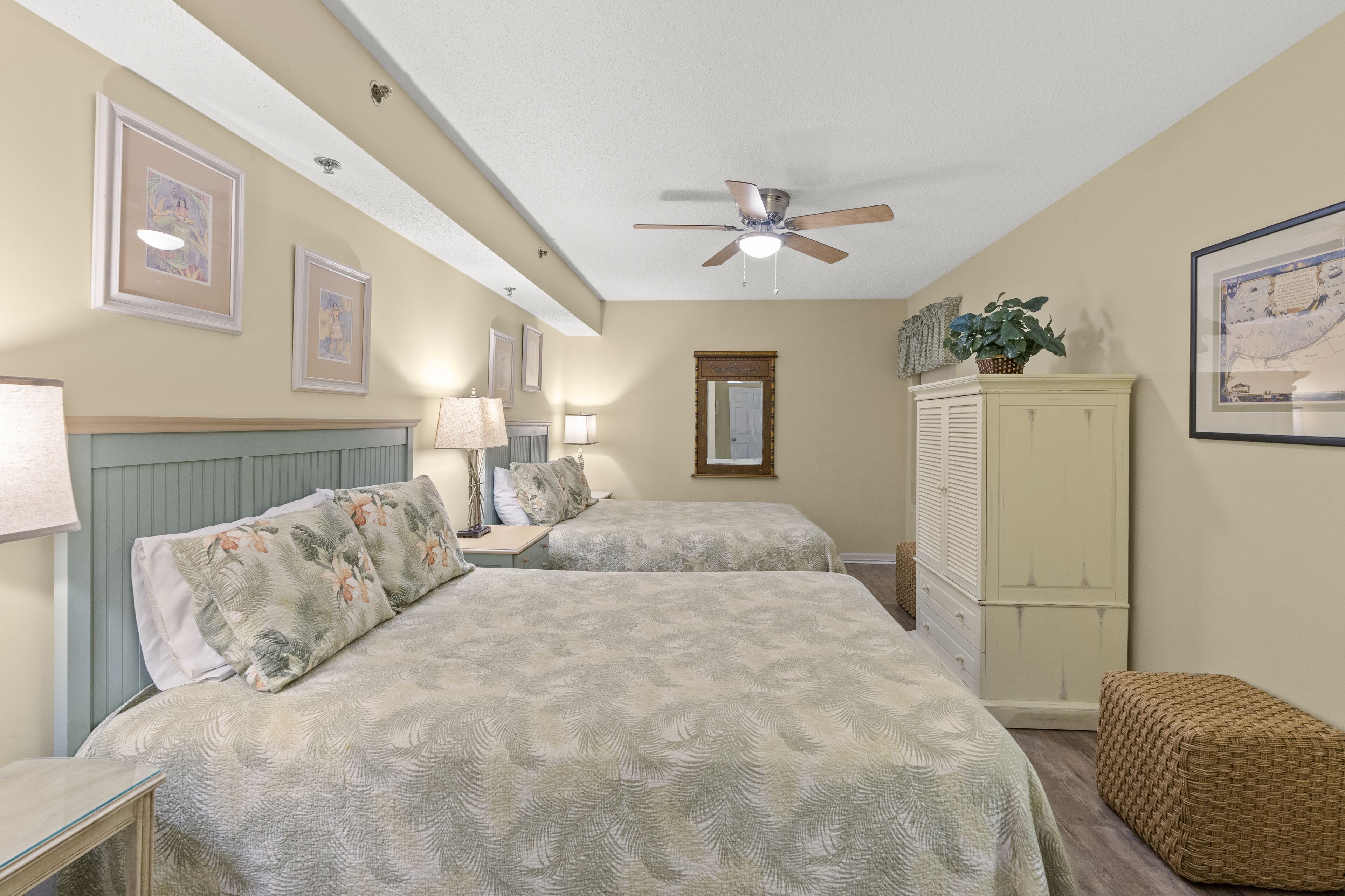 Une chambre avec deux lits, un ventilateur de plafond, une armoire et des œuvres d’art encadrées accrochées aux murs.
