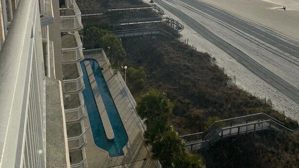 Een hoog hotel met een zwembad, uitzicht op het strand en een promenade naar de kust.