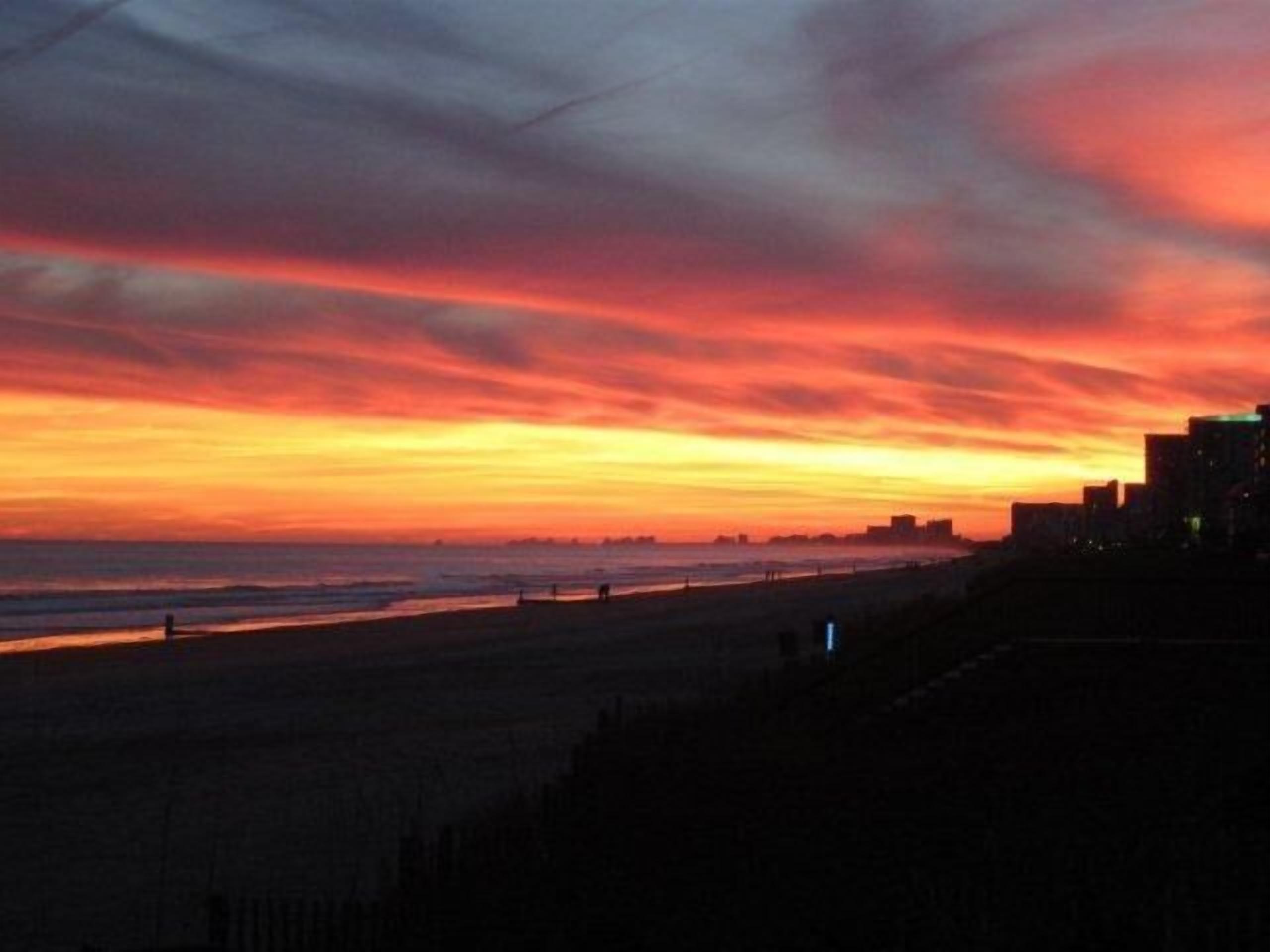 Una playa con un atardecer y el perfil urbano al fondo.