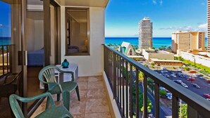 A balcony with a view of the ocean and cityscape, a table with chairs, and a small table with a decorative item.