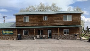 A two-story log cabin with a stone foundation, a green metal roof, and a sign advertising sheepsheds.