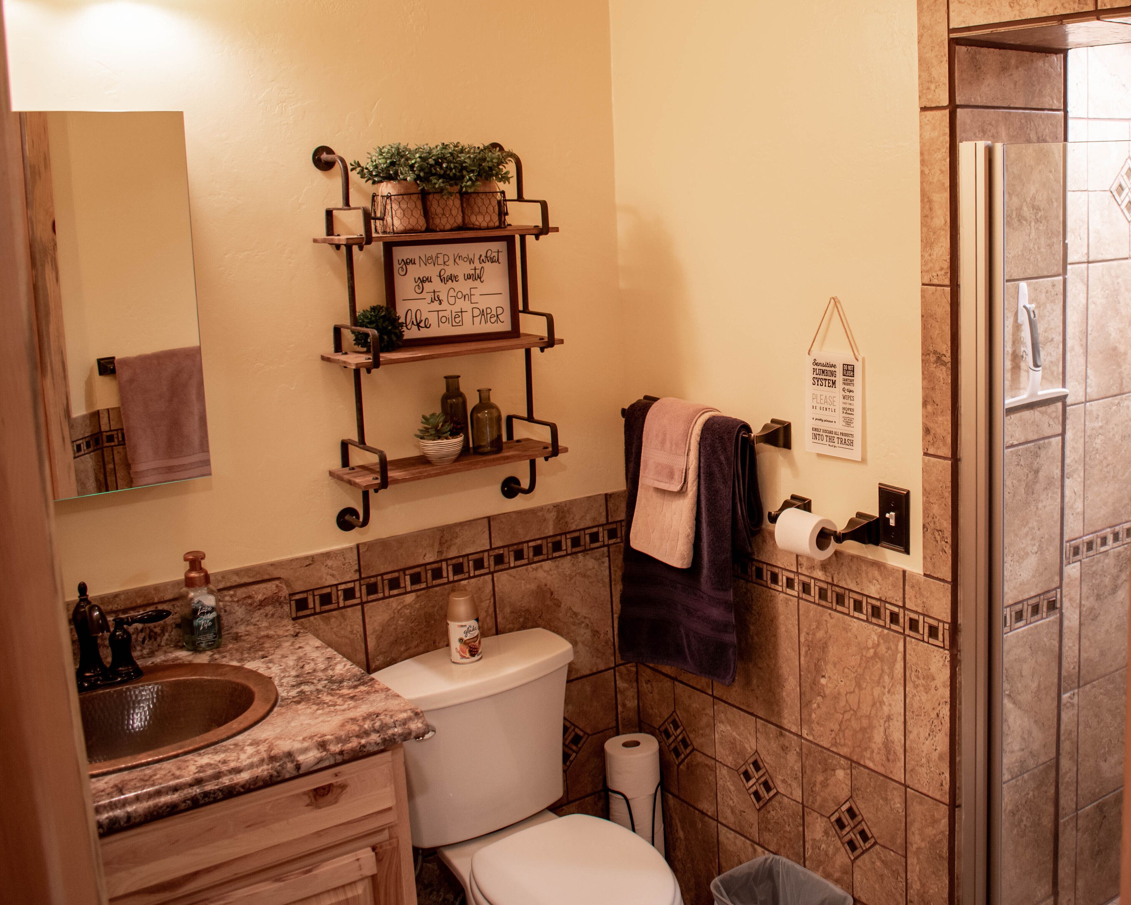 Une salle de bain équipée de toilettes, d’un lavabo et d ’étagères contenant des articles de toilette. Il y a un panneau sur le mur et un porte-serviettes.