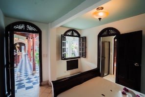Una habitación con una cama, un espejo y una puerta que da a un pasillo con piso a cuadros.