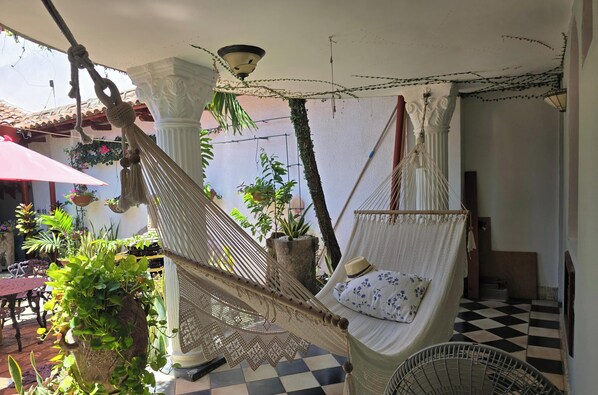 Una silla hamaca con cojín, un adorno colgante de macramé y plantas en macetas.