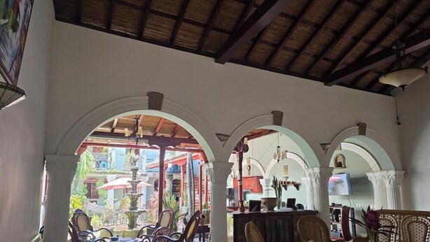 A covered outdoor seating area with arches, a fountain, and a view of a colorful building. - Casa Don Carlos a Gorgeous Colonial House! (Granada)