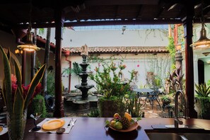 Een terras met een eettafel voor twee personen, een stenen fontein en verschillende planten.