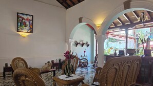 A room with wicker furniture, a large painting, and a view through an archway. - Casa Don Carlos a Gorgeous Colonial House! (Granada)