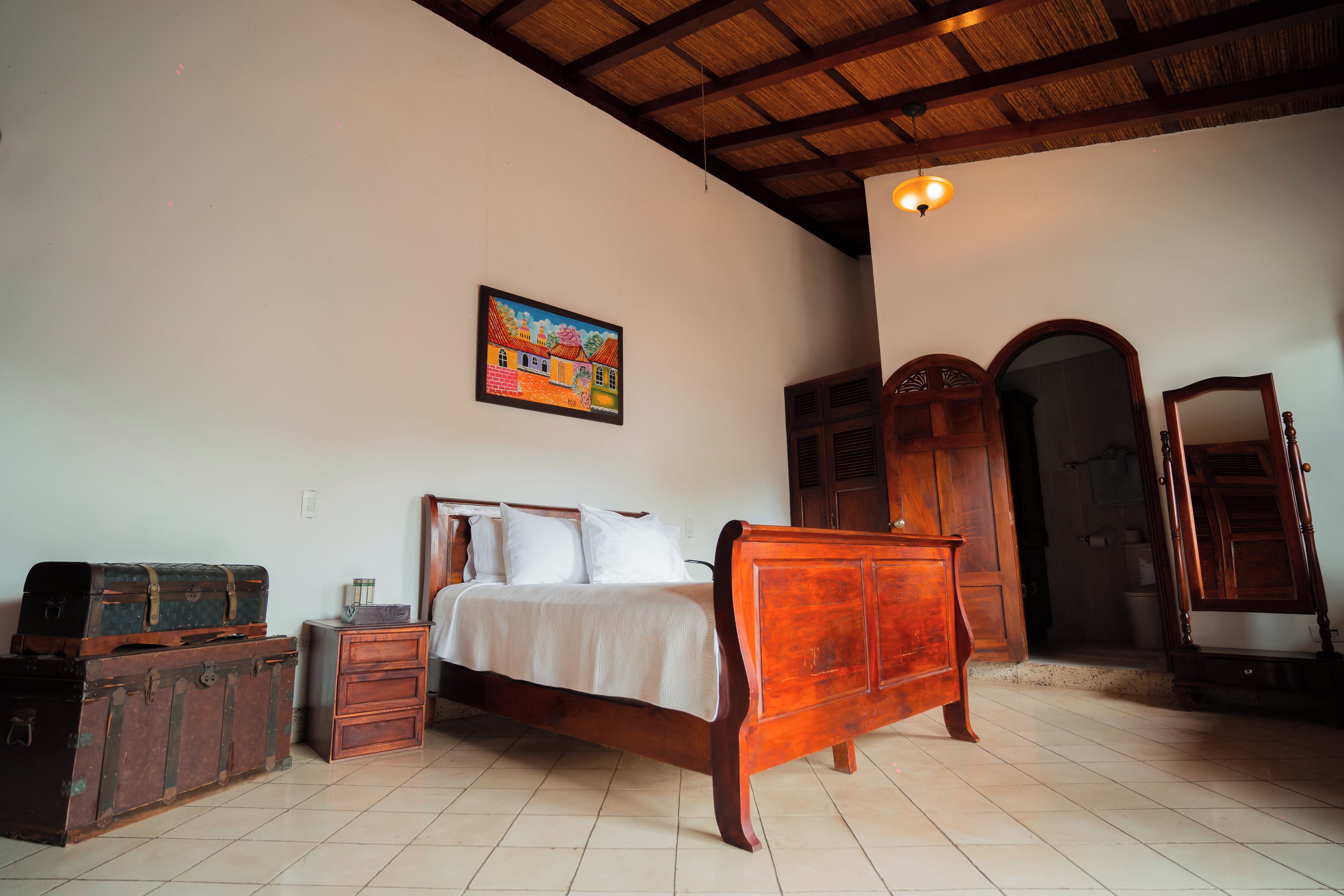 Une chambre à coucher avec un lit en bois, une table de chevet, une commode et un tableau accroché au mur.