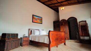 Une chambre à coucher avec un lit en bois, une table de chevet, une commode et un tableau accroché au mur.
