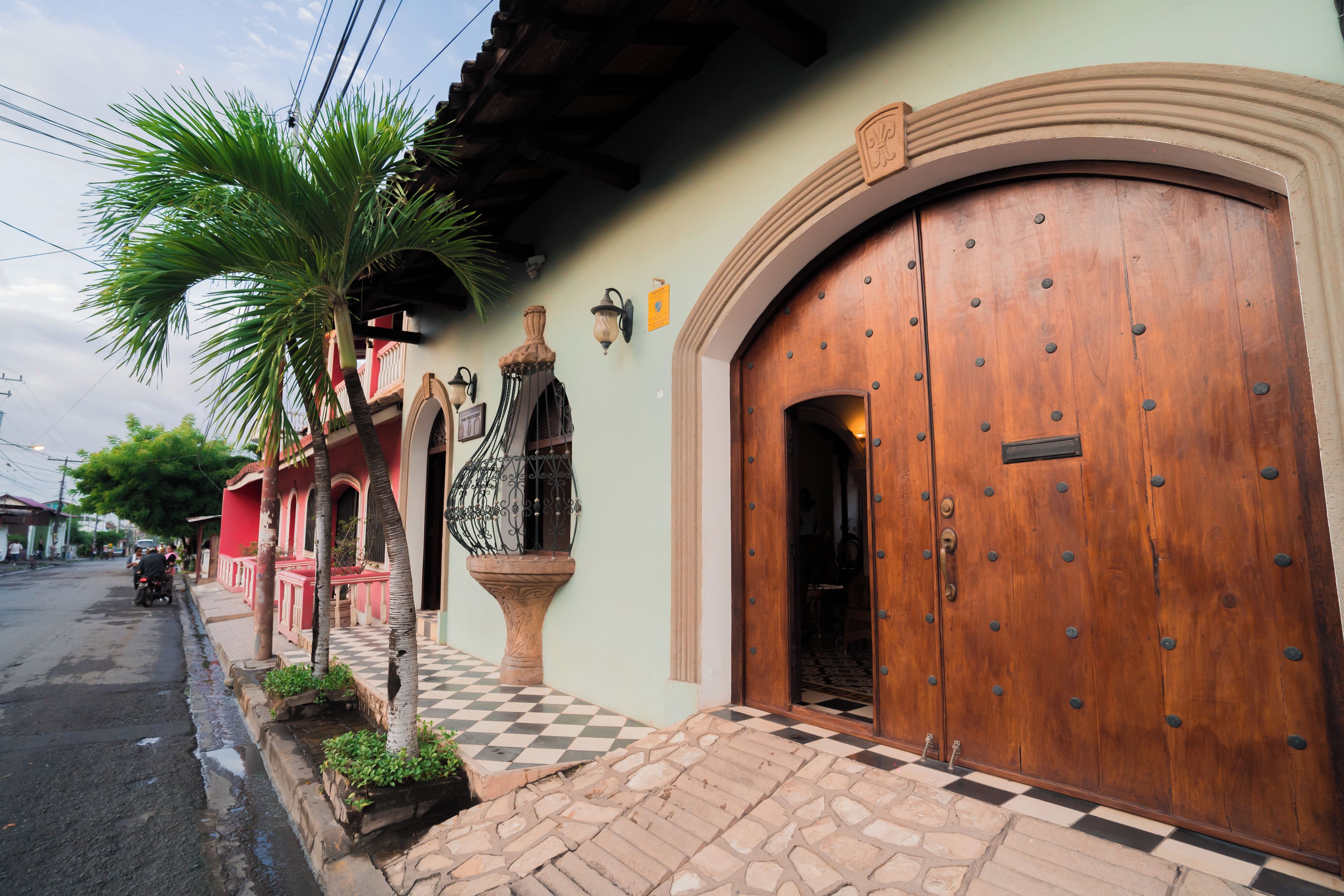 Un edificio con una puerta de madera grande, piso a cuadros y una palmera.