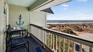 Een balkon met uitzicht op het strand, een tafel met stoelen en een decoratief anker.