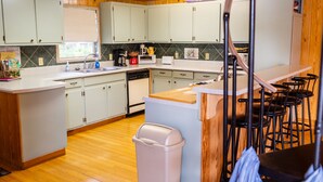 A kitchen with white cabinets, a dishwasher, a coffee maker, and a trash can. - Tifton, GA - Shalom Guest House - Cabin in Peaceful Setting (Tifton)