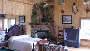 A cozy room with a bed, a fireplace, a pool table, and mounted animal heads on the wall. - Tifton, GA - Shalom Guest House - Cabin in Peaceful Setting (Tifton)