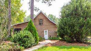 A log cabin with a wooden exterior, a front door, and a small window. - Tifton, GA - Shalom Guest House - Cabin in Peaceful Setting (Tifton)