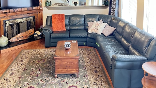 Ein Wohnzimmer mit einem schwarzen Ledersofa, einem Holztisch, einem gemusterten Teppich und einer Holzzieldecke.