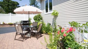 Une terrasse extérieure avec une table et des chaises, un barbecue et un parasol blanc.