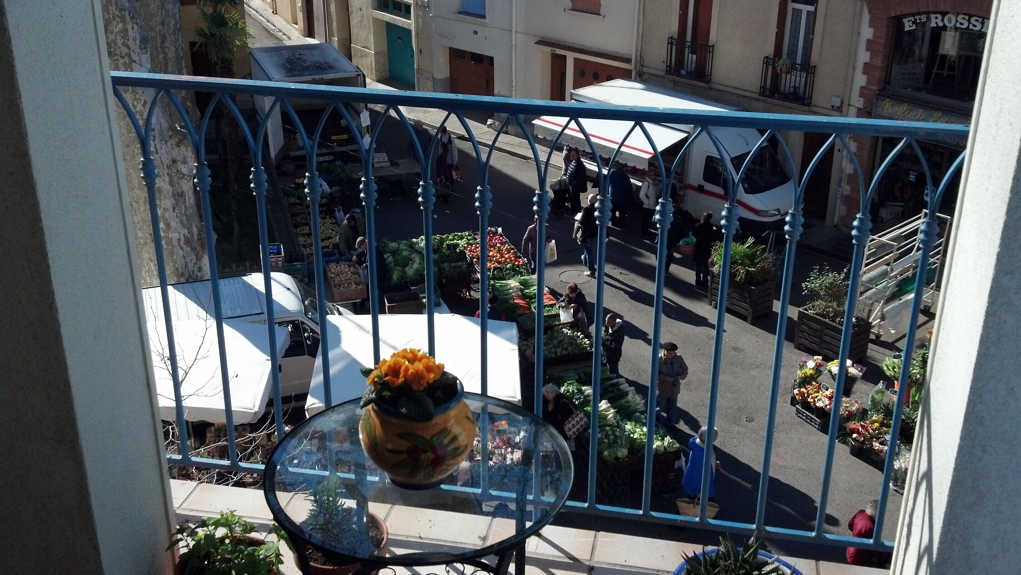 A balcony with a view of a street market, a potted plant, and a white van.