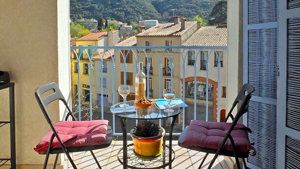 A balcony with a table, chairs, and a view of a mountain and buildings.