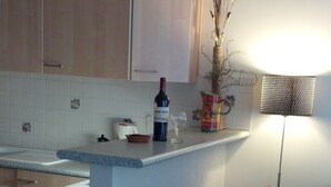 A kitchen with wooden cabinets, a small island, a wine bottle, a vase with dried branches, and a chair.