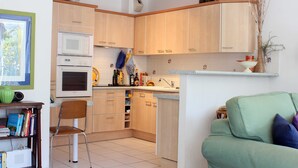 A compact kitchen with wooden cabinets, a built-in oven, and a dining area with a chair and table.